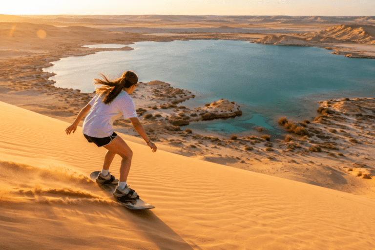 Teenage girl sandboarding down a large golden dune overlooking Magic Lake