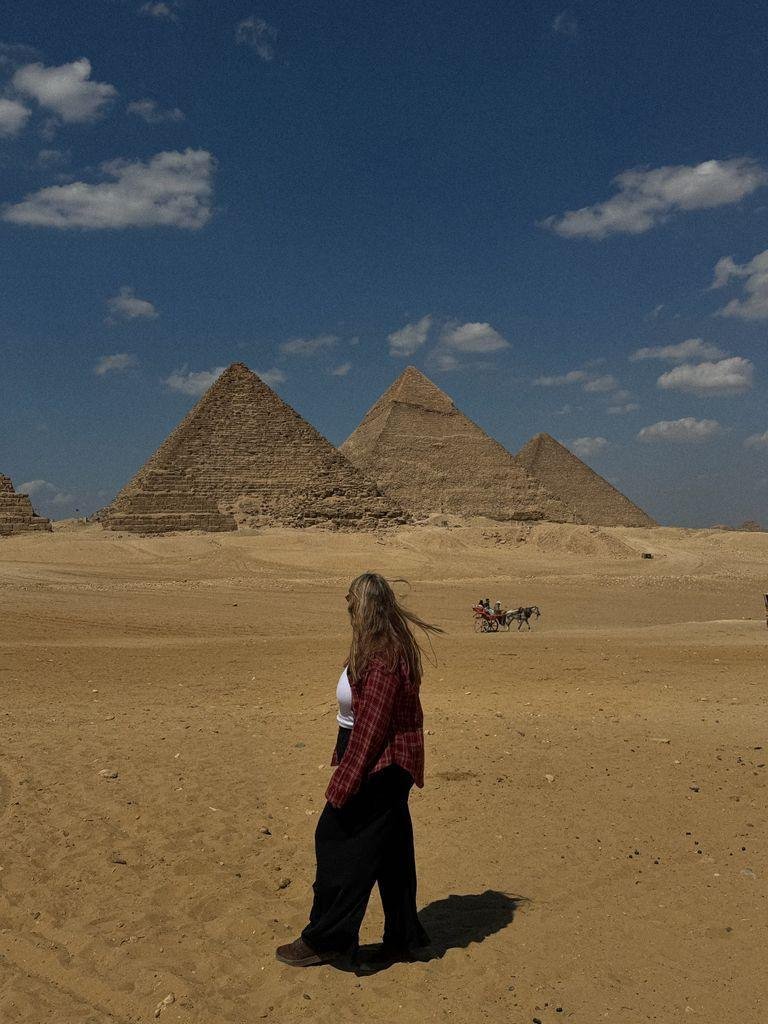 A tourist explores the iconic Pyramids of Giza, Egypt, capturing the ancient wonder under a bright blue sky.