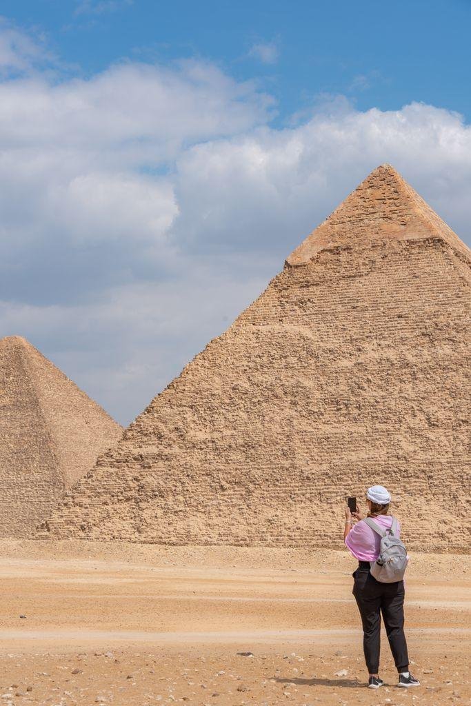A woman photographs the stunning Pyramids of Giza under a clear blue sky.