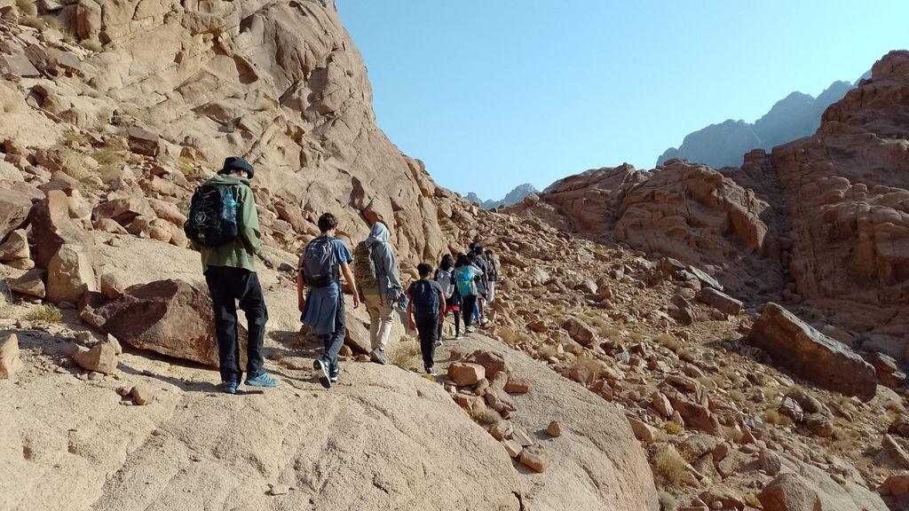 Group hiking on a rocky path in Saint Catherine, Egypt under clear skies.
