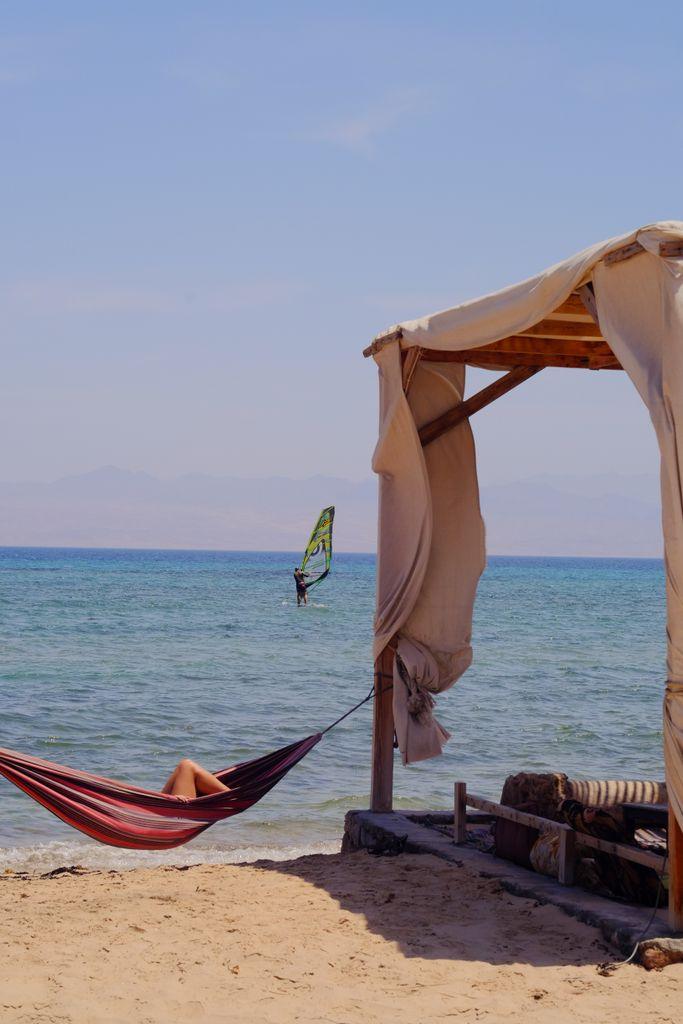 Serene beach scene with hammock and windsurfer in Nuweibaa, Egypt.
